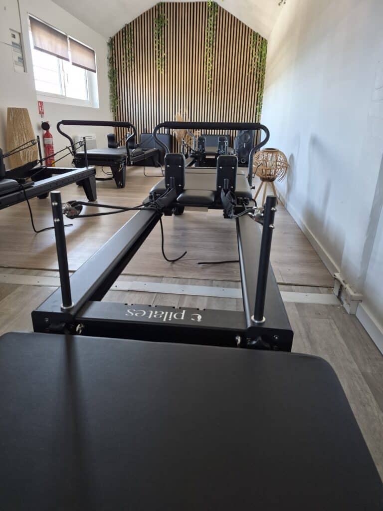 Studio Pilates Reformer : Équipements Professionnels Zen Reformer noir marqué pilates dans un studio moderne au mur en tasseaux de bois et décoration naturelle.